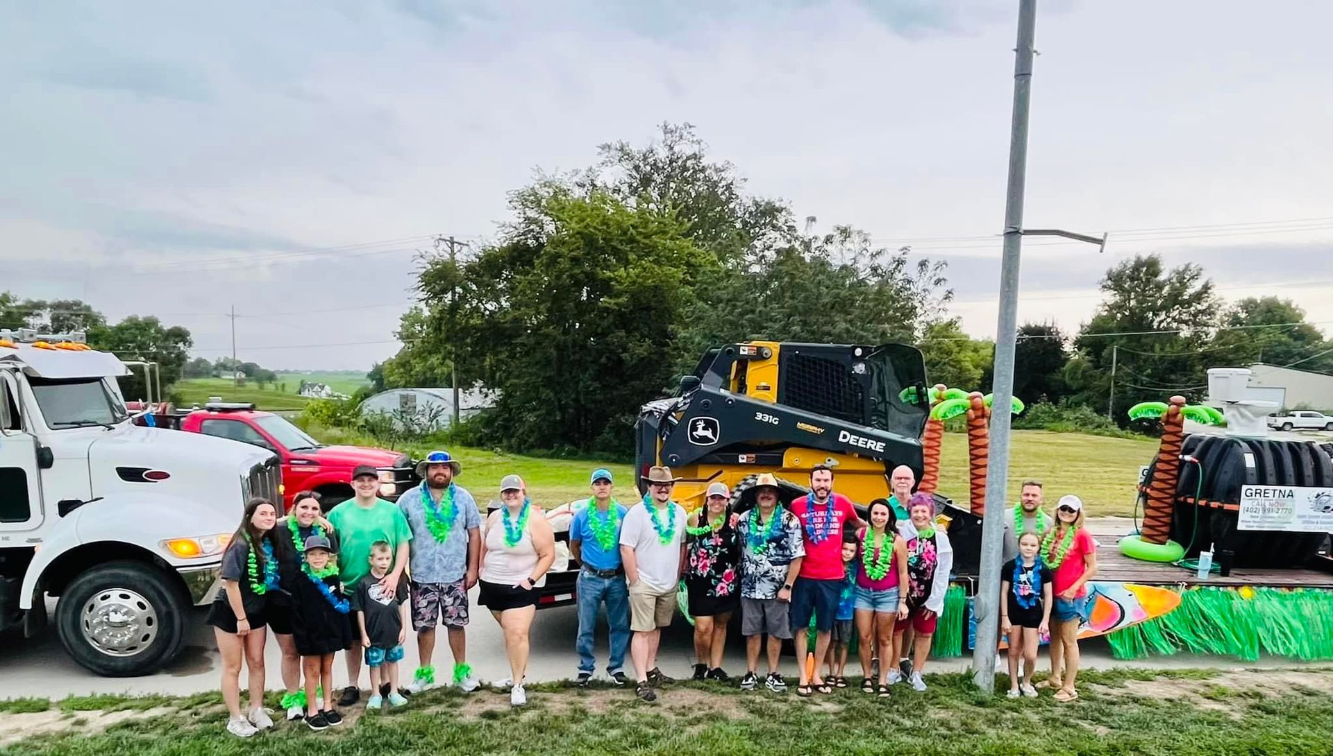 Group of people posing with floats and a construction vehicle in an outdoor setting.