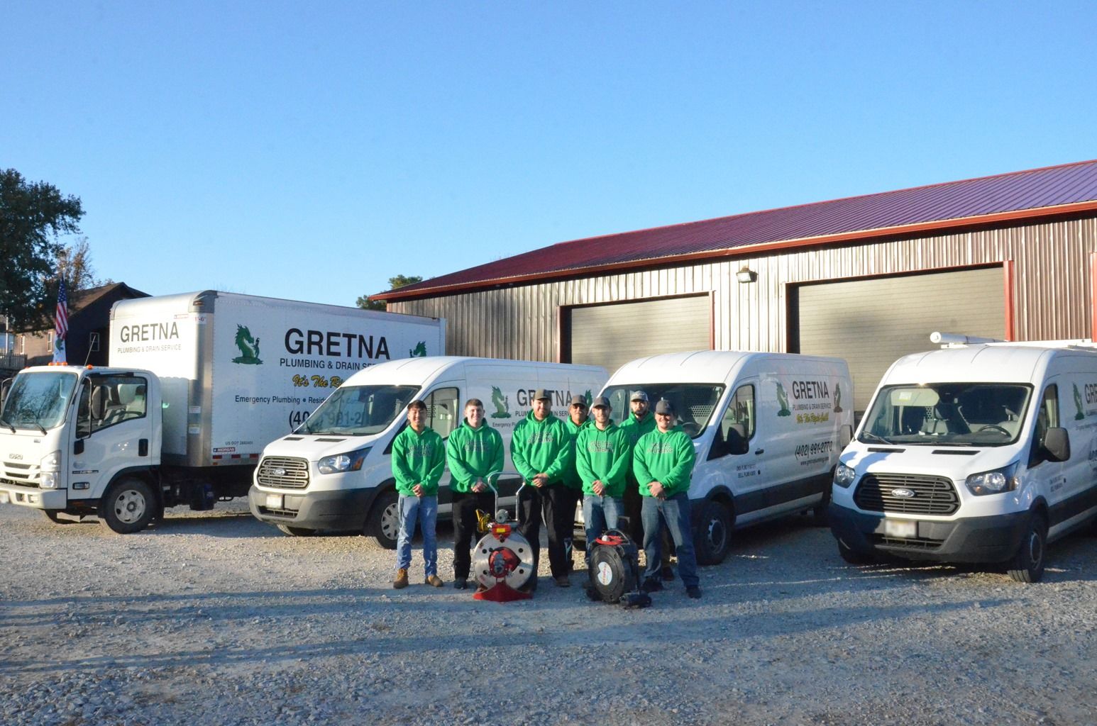 Gretna Moving staff pose with company trucks outside a building. They wear green shirts, holding a dolly.
