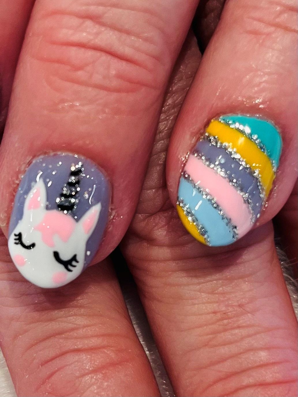 A close up of a person's nails with unicorn and horizontal color designs
