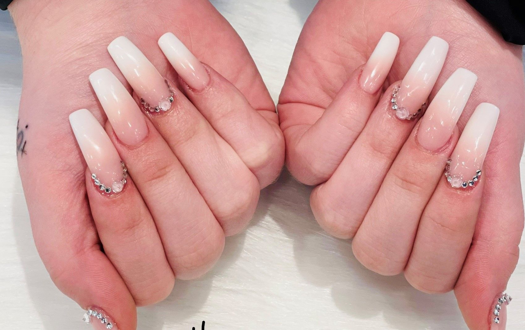A woman's hands with long white nails and rhinestones on them