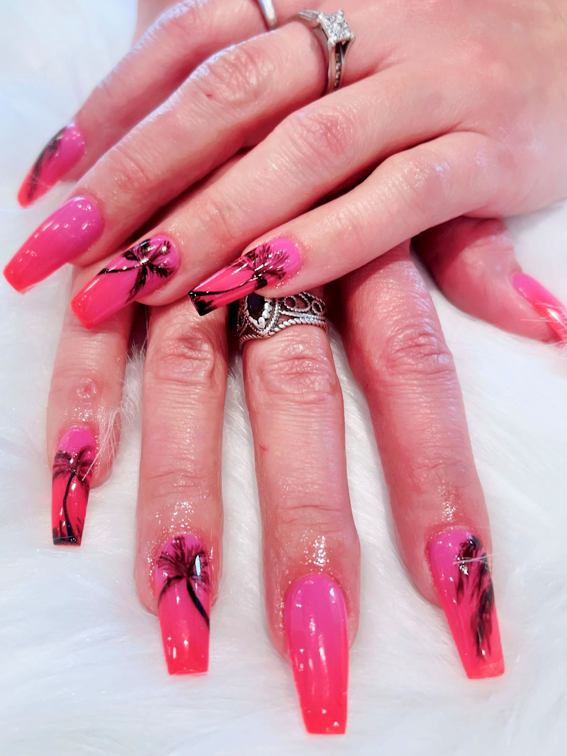A close up of a woman's nails with a pink polish and palm tree design