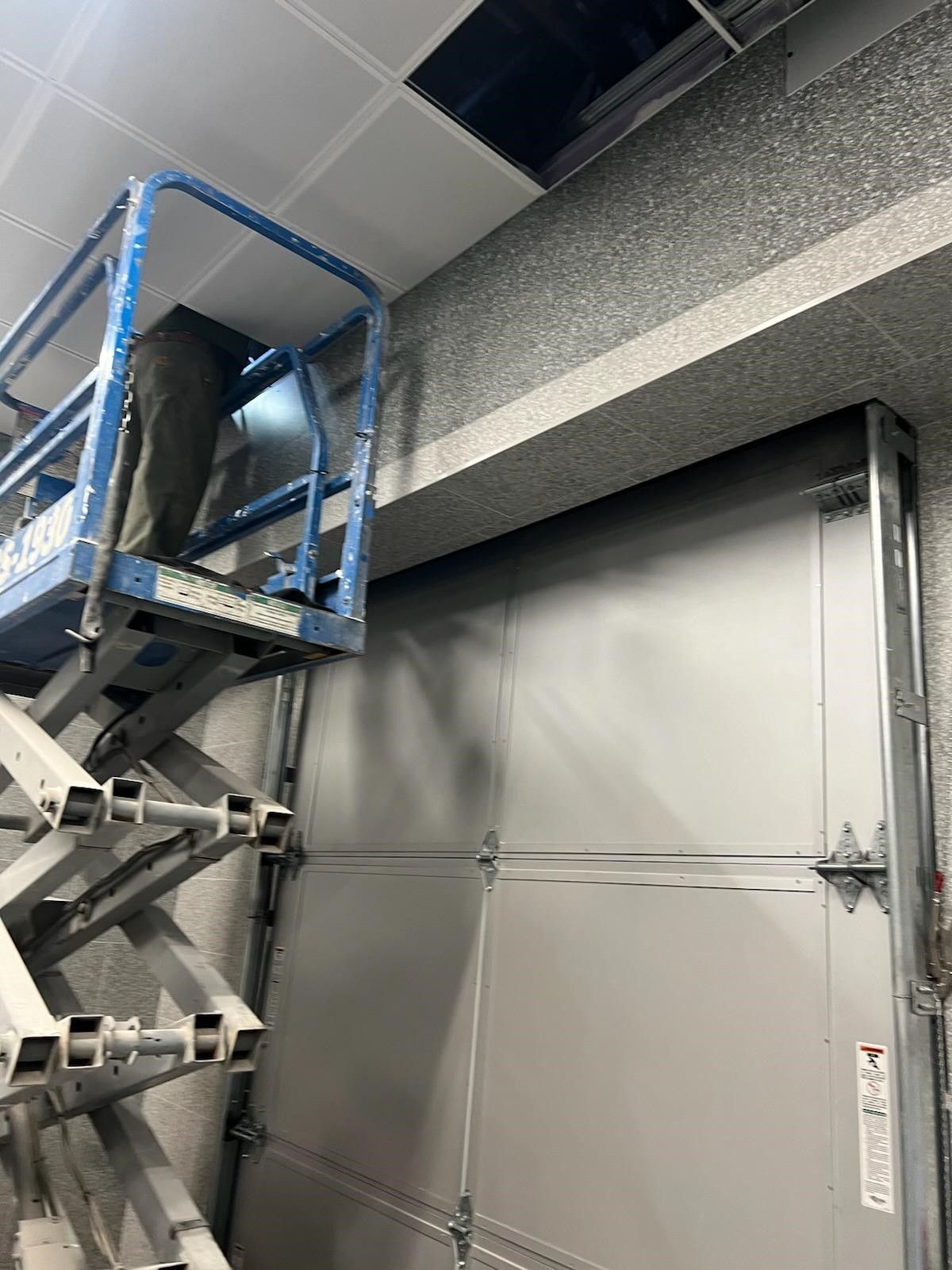 A man is standing on a scissor lift next to a garage door.