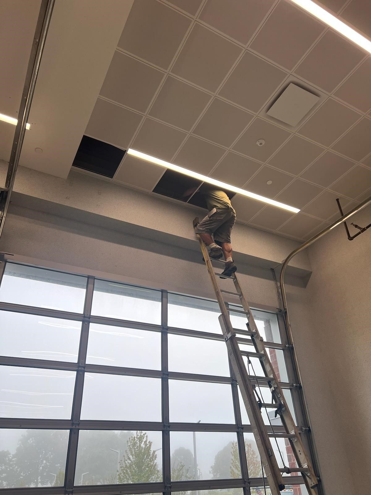 A man is standing on a ladder looking through a hole in the ceiling.