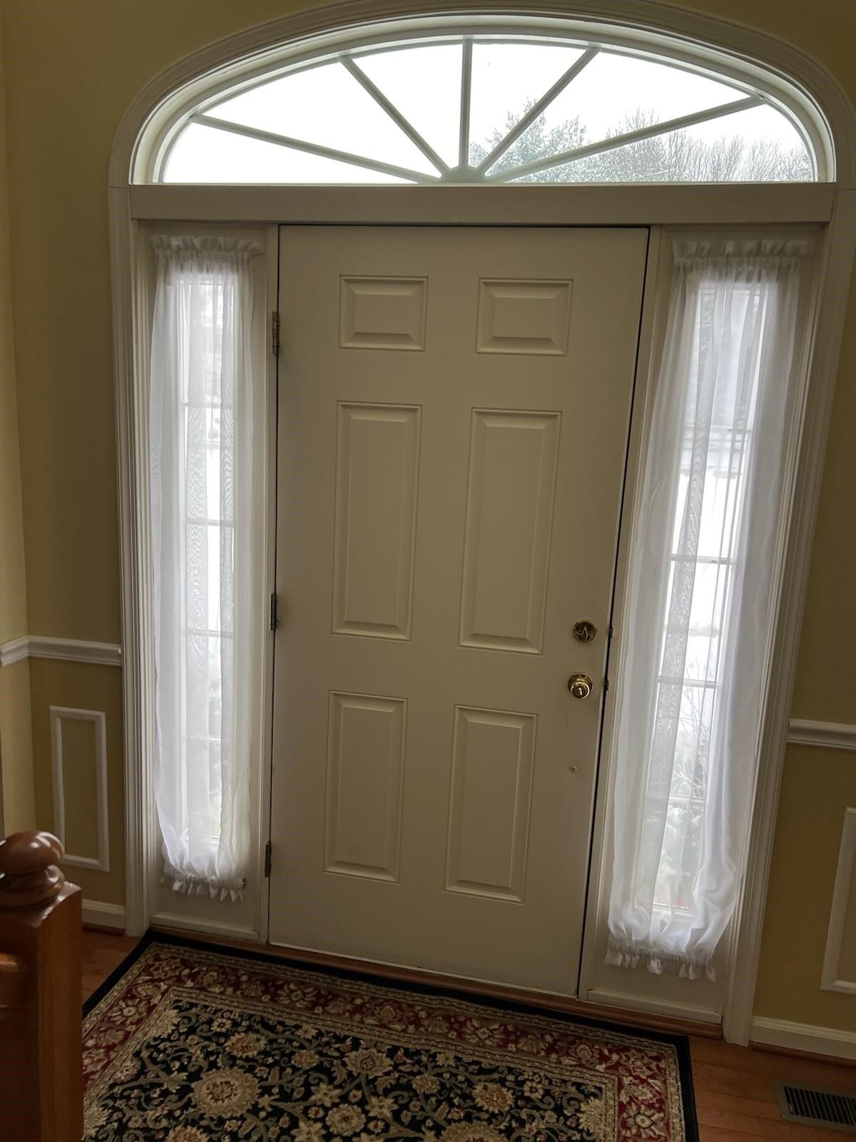 A white door with white curtains and a window in a house.