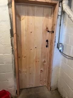 A wooden door is in a basement next to a brick wall.