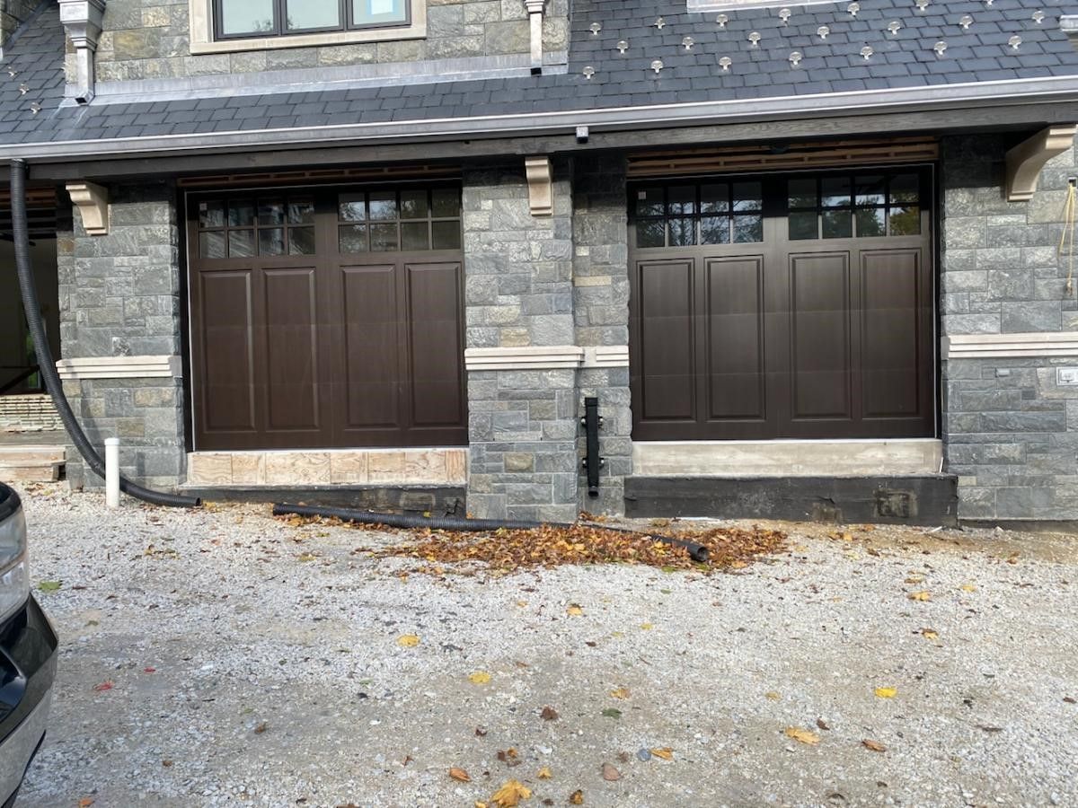 A car is parked in front of a house with two garage doors.