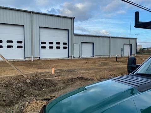 A green truck is parked in front of a building with white garage doors.