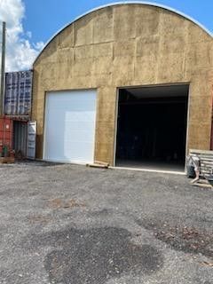 A large warehouse with a large white door is sitting in the middle of a parking lot.