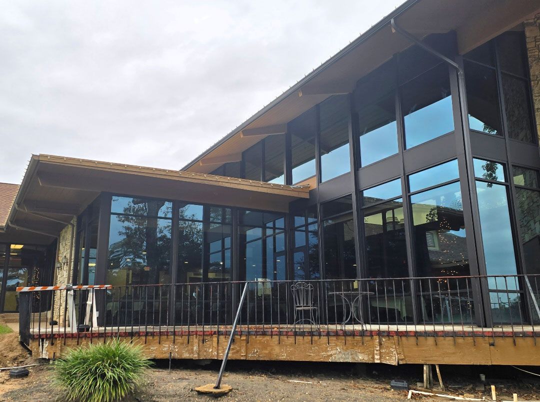 A low-angle view of a modern building with large, reflective glass windows, dark metal framing, and a wooden deck.