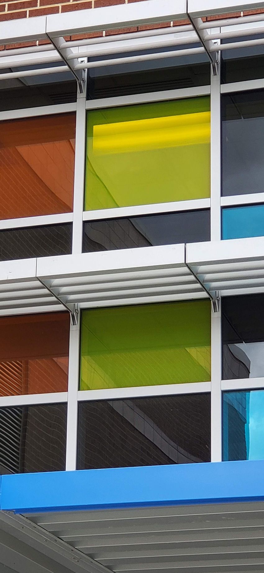 A close-up view of a building facade with rectangular windows featuring orange, yellow, and blue panels and sun shades.