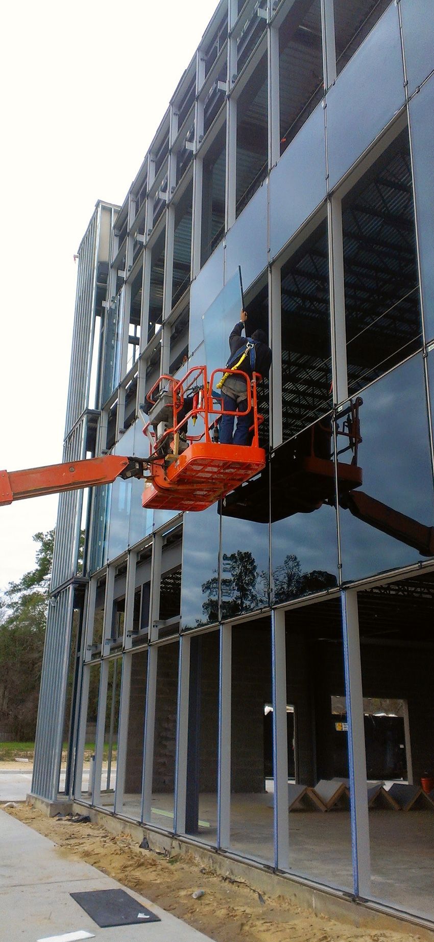Workers in an orange boom lift install glass panels on the facade of a multi-story building under construction.
