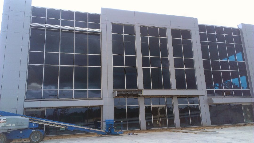 A modern, multi-story commercial building under construction with a large glass facade and gray structural columns.