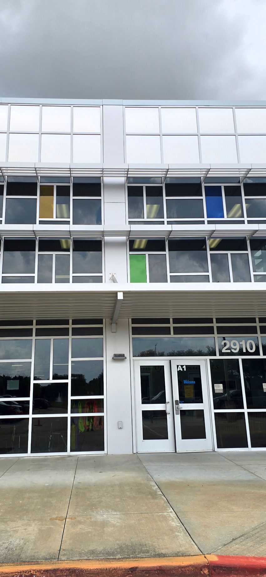 A two-story commercial building exterior with white trim, large glass windows, and a set of double entry doors labeled 2910.