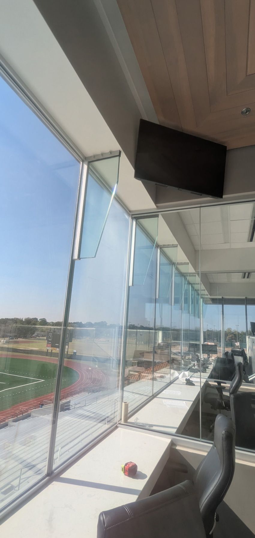 A bright office with floor-to-ceiling windows overlooking a sunny outdoor sports field, featuring modern desk chairs.