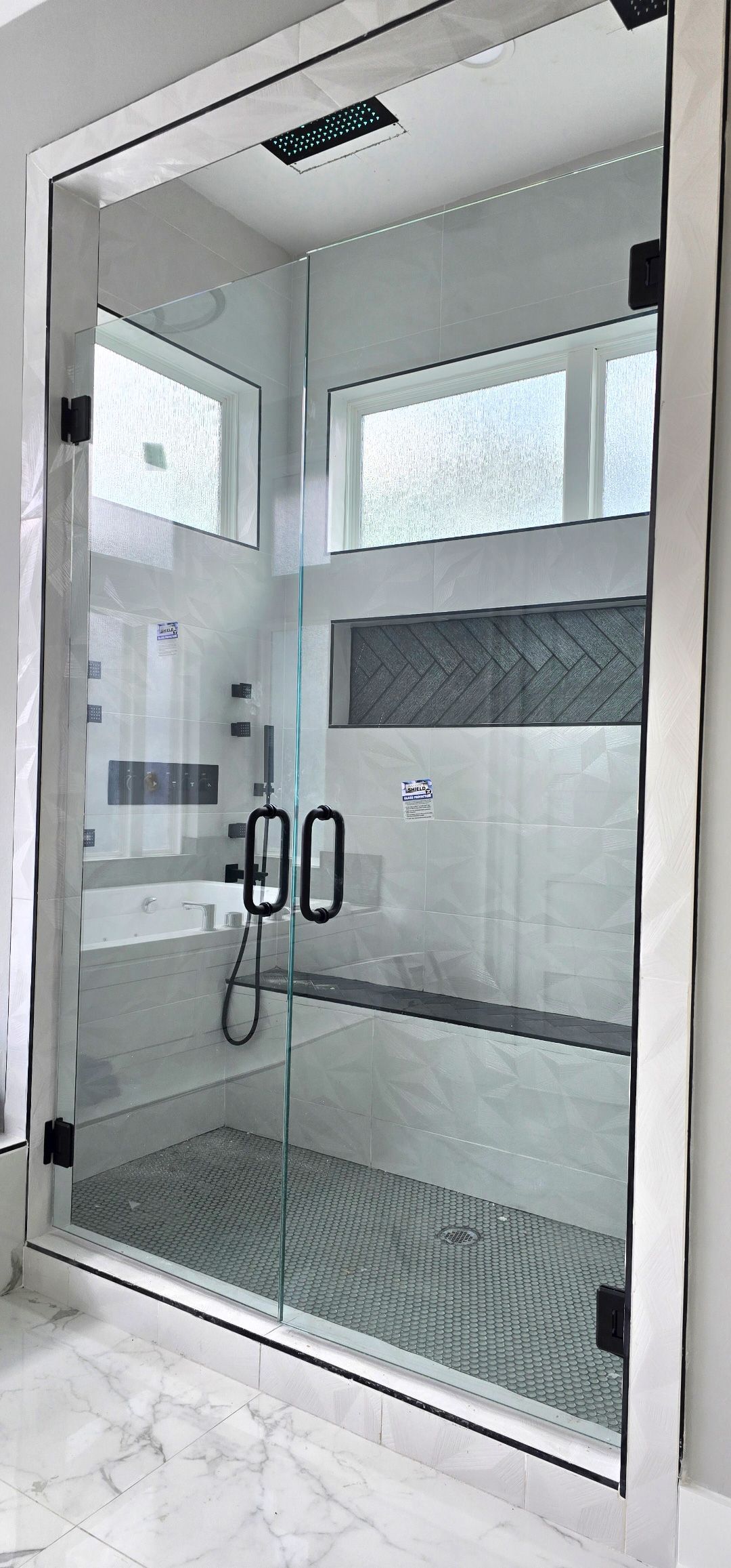 A neutral-toned bathroom with a freestanding white tub, tiled wall, double vanity with black countertop, and large mirror.
