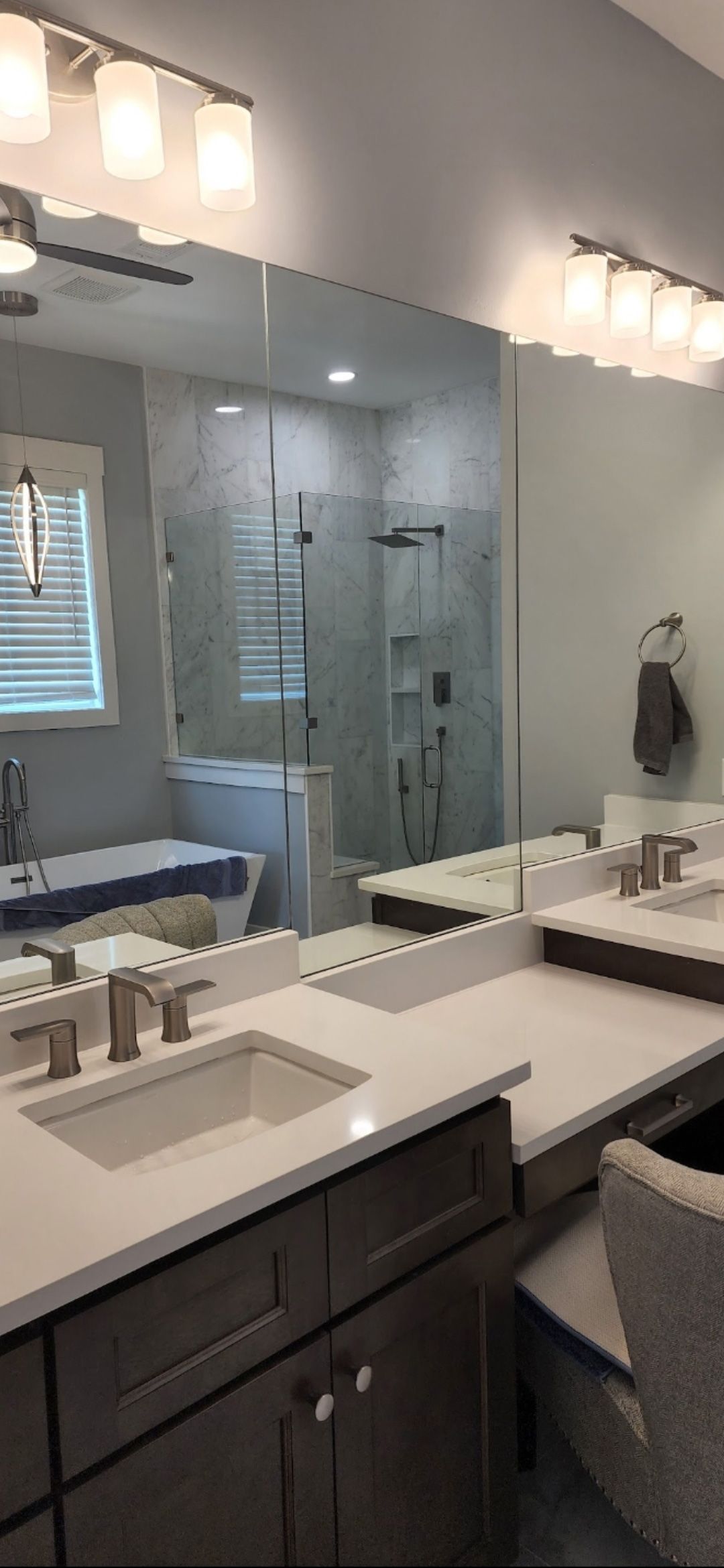 A modern bathroom vanity with double sinks, quartz countertops, dark cabinets, and large mirrors reflecting a shower.