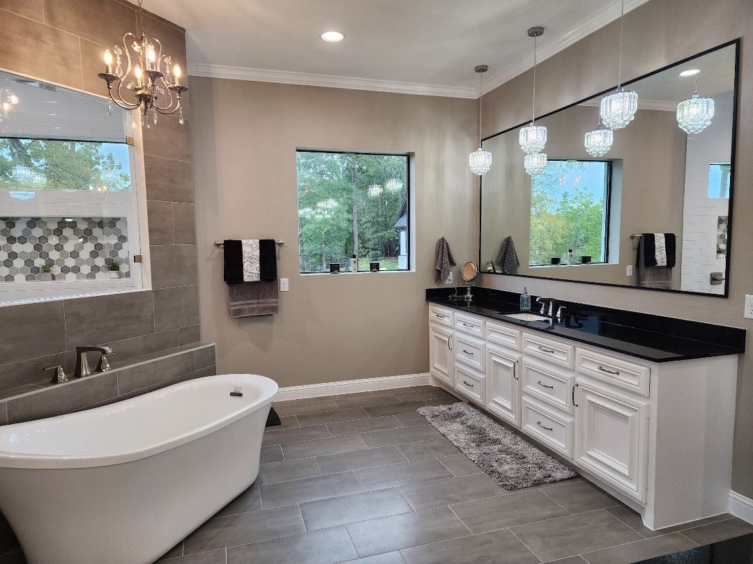 A modern bathroom featuring a white freestanding tub, a long double vanity with black countertops, and a large wall mirror.