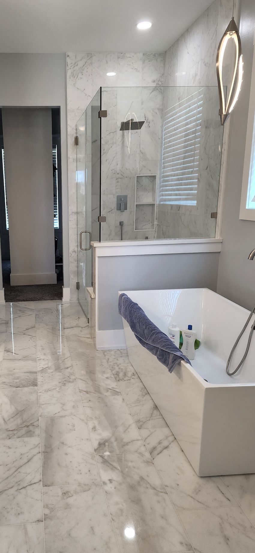 A modern bathroom featuring a white soaking tub, glass-enclosed marble shower, and light gray tile flooring.