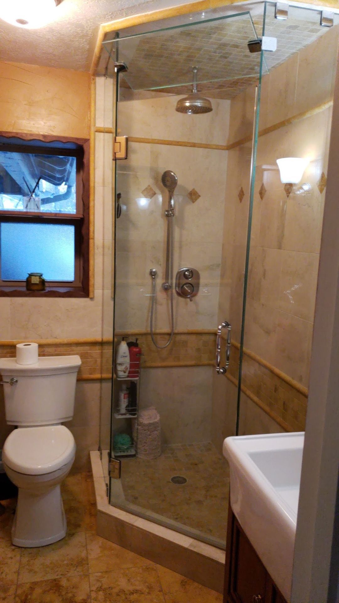 A bathroom featuring a glass shower stall, a white toilet, and a vanity, all tiled in neutral, warm-toned stone.