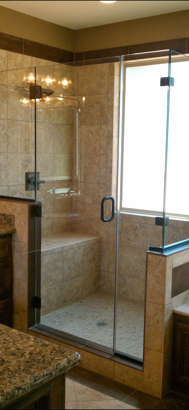 A glass-enclosed walk-in shower with light brown tiled walls and a built-in stone bench seat.