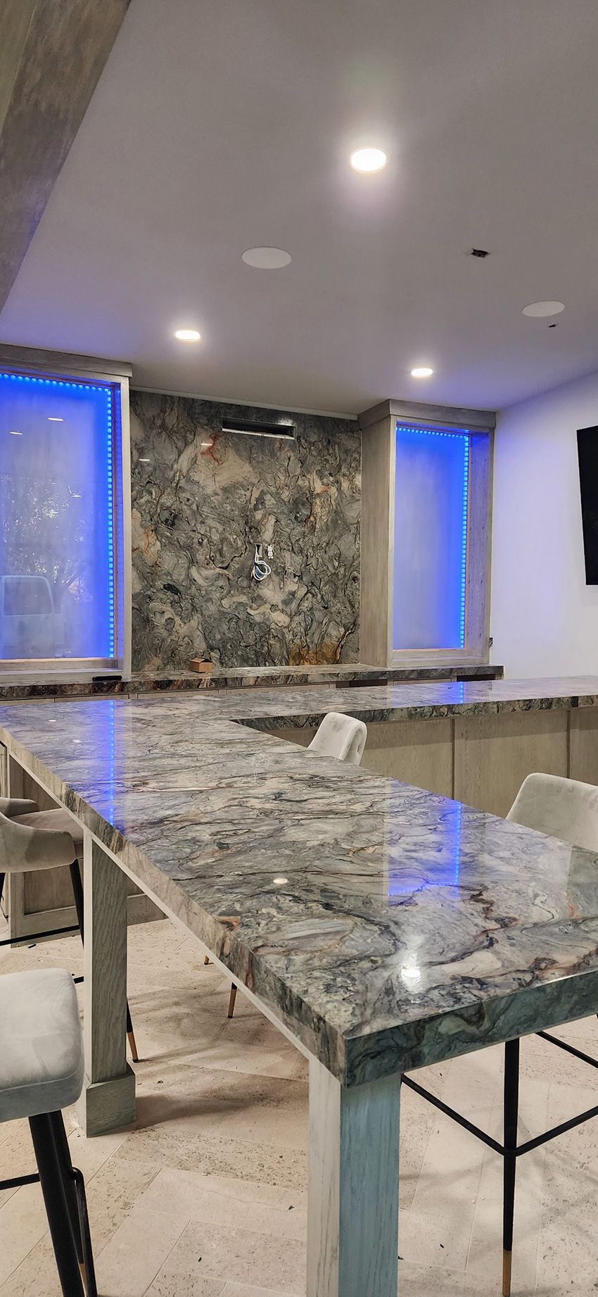 A high-top bar with a granite countertop and matching backsplash, featuring blue accent lighting in a modern room.