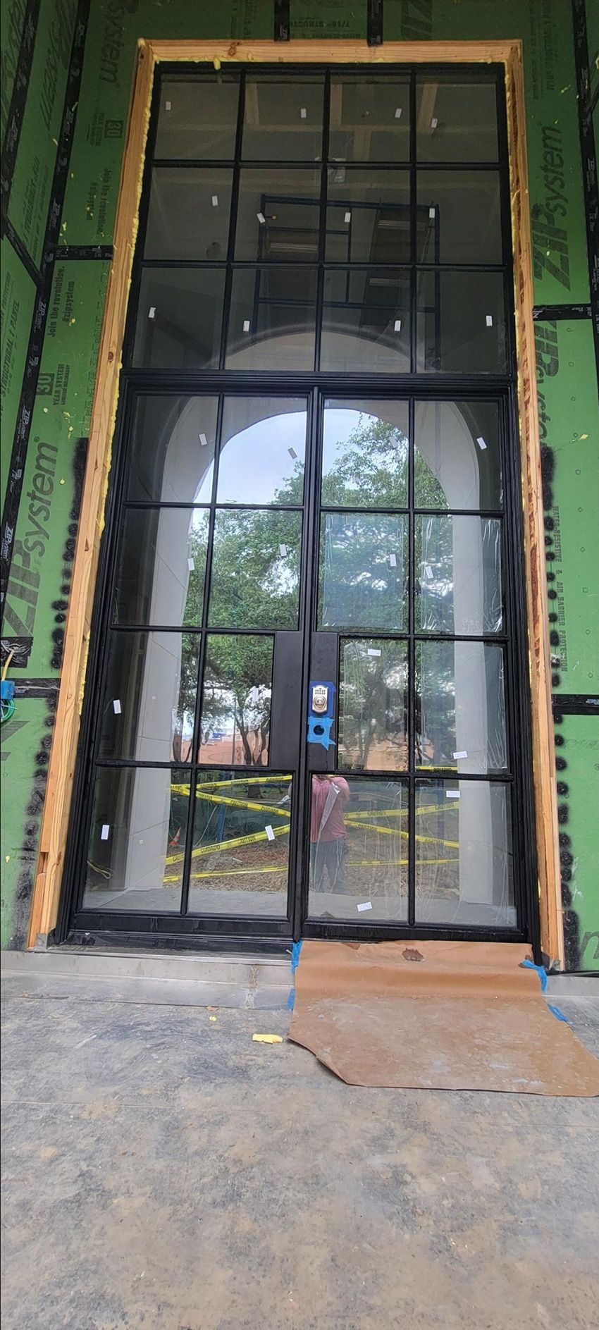 Large black grid-style double door with glass panels set into a building exterior with green sheathing.