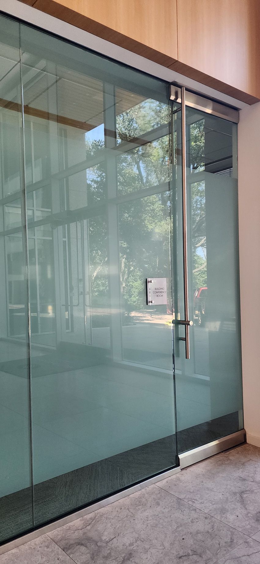 A glass door with a tall silver handle and a small square sign, set in a modern building entrance.
