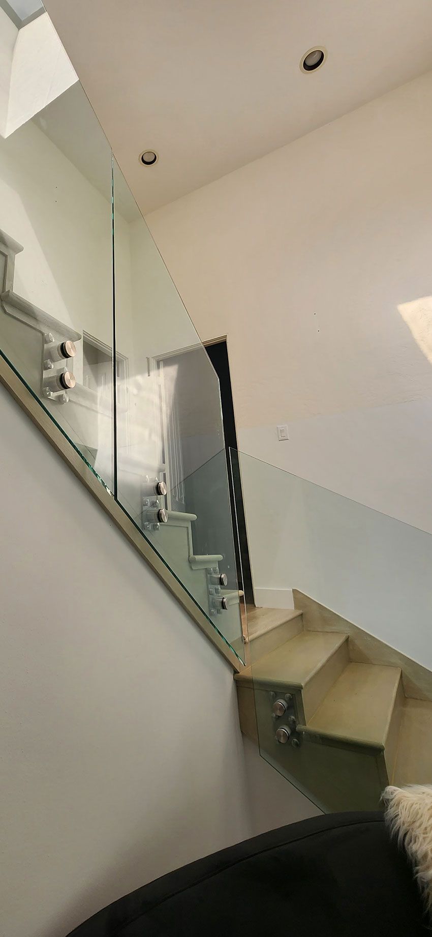 A staircase with light-colored wooden steps and a frameless glass railing mounted with metal clamps.