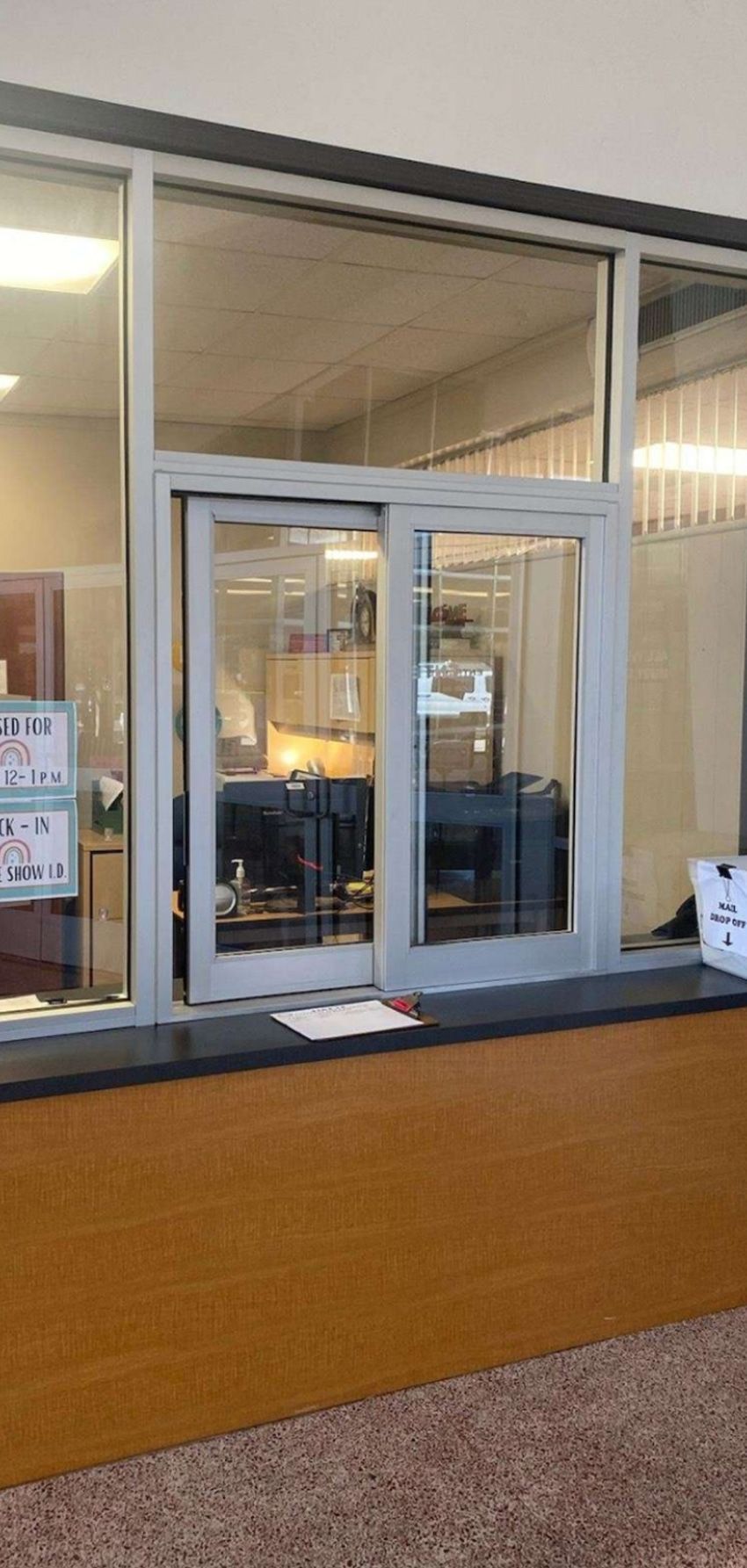 A customer service window featuring a gray frame, glass panels, and a counter in a beige-walled room.