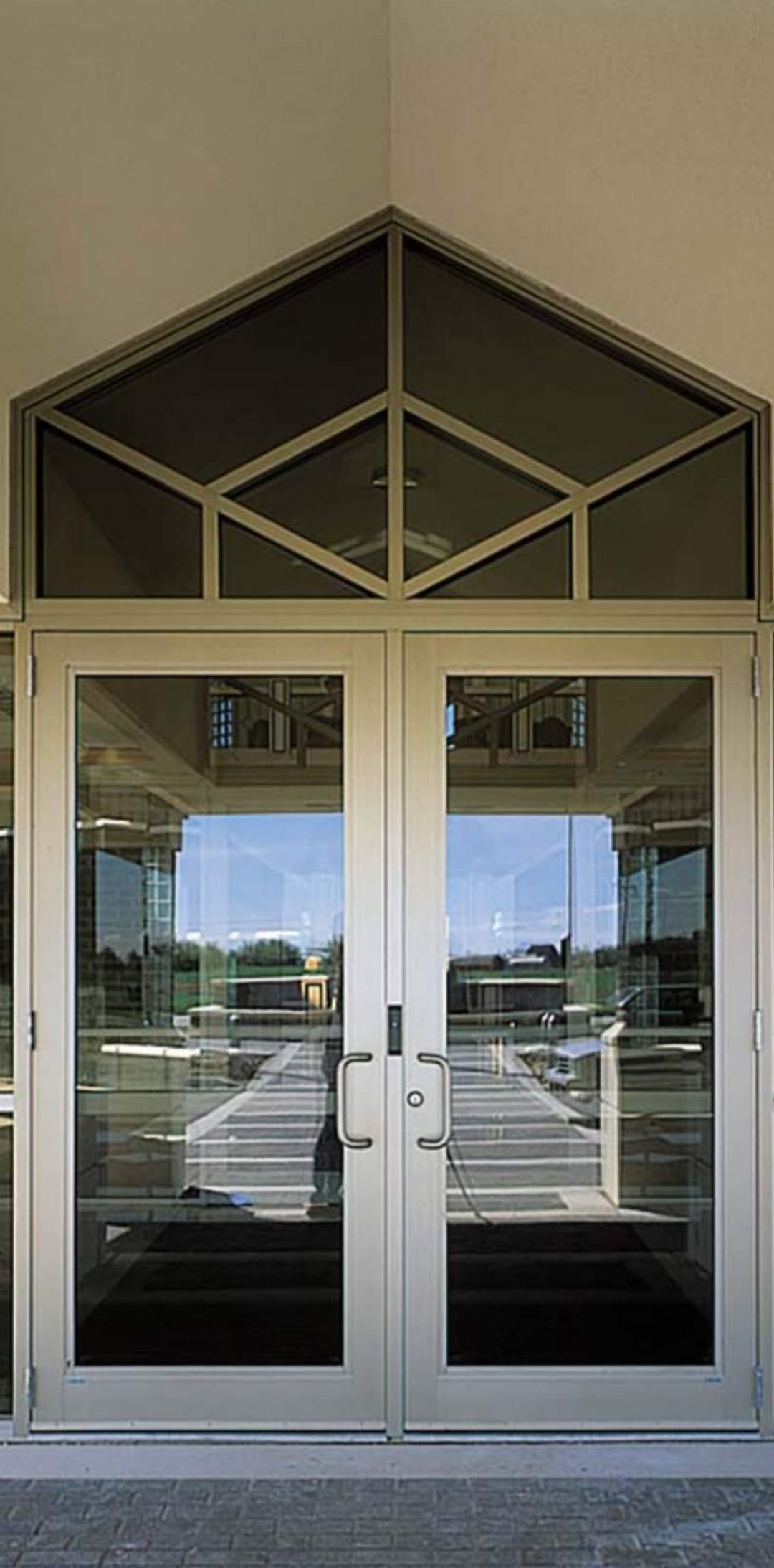 Double glass doors framed in light metal with a geometric, triangular transom window above.