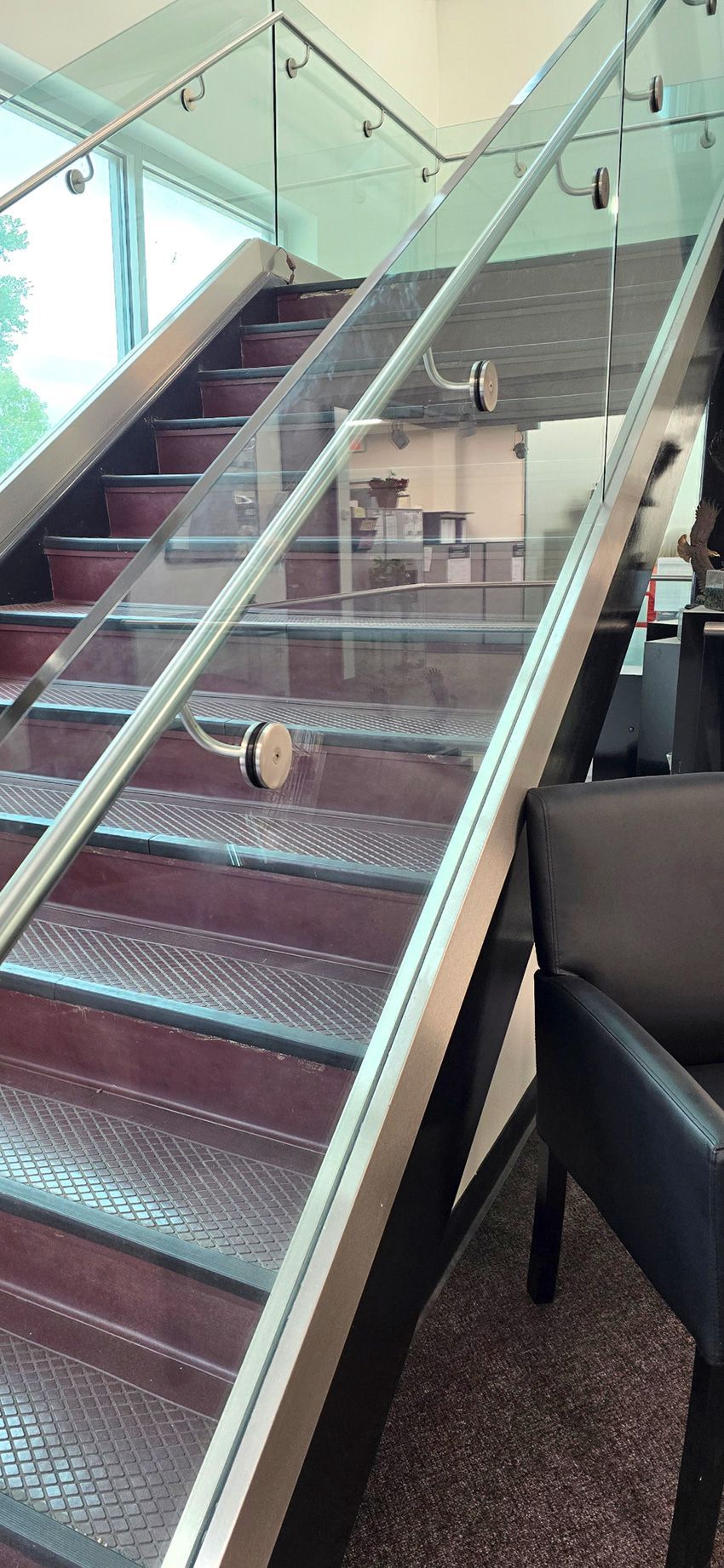 A staircase with metal diamond-plate steps, dark risers, and a glass railing with stainless steel hardware.