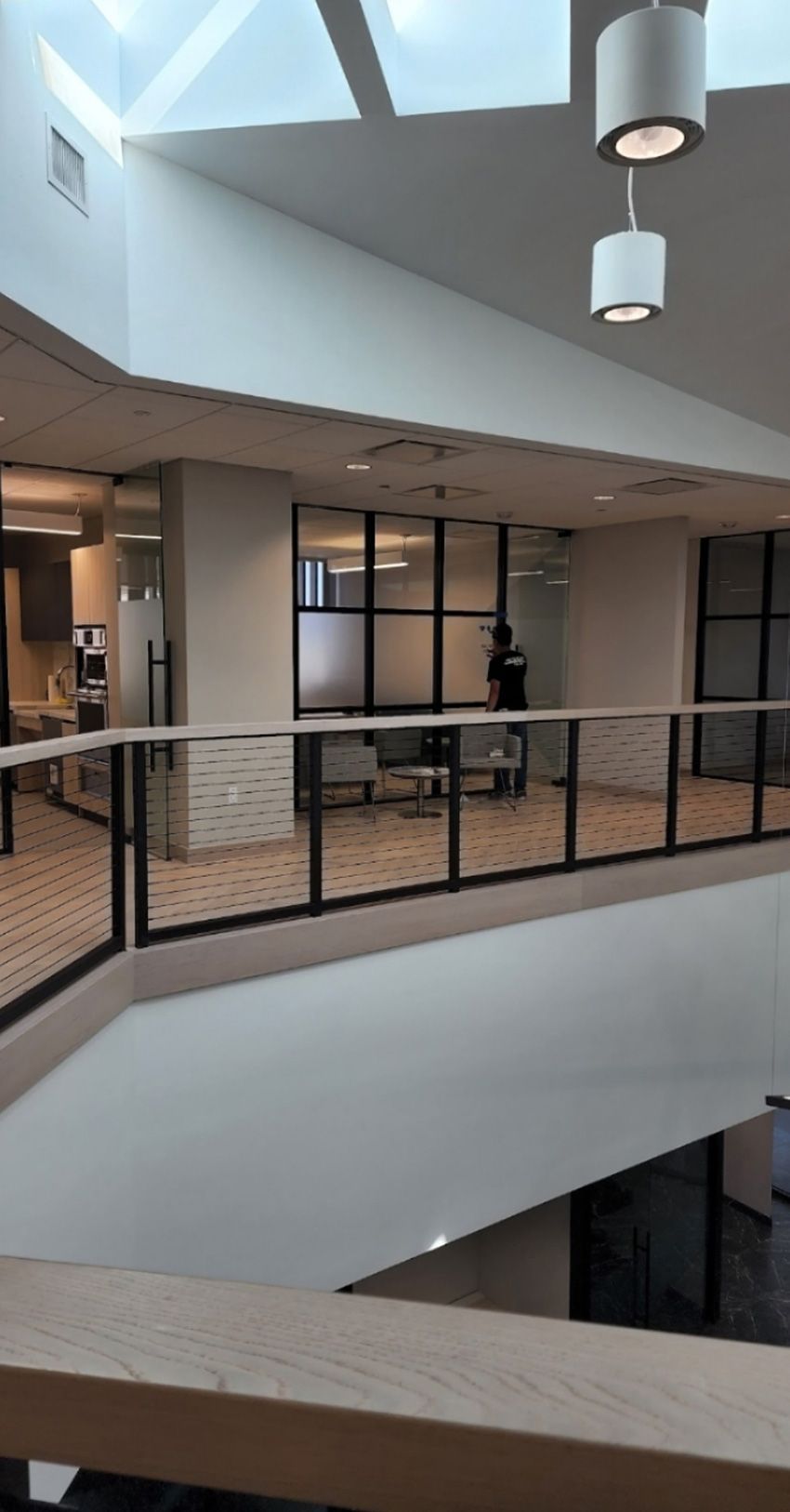 A high-angle view of a modern building interior featuring a loft balcony with glass railings, pendant lights, and a desk.