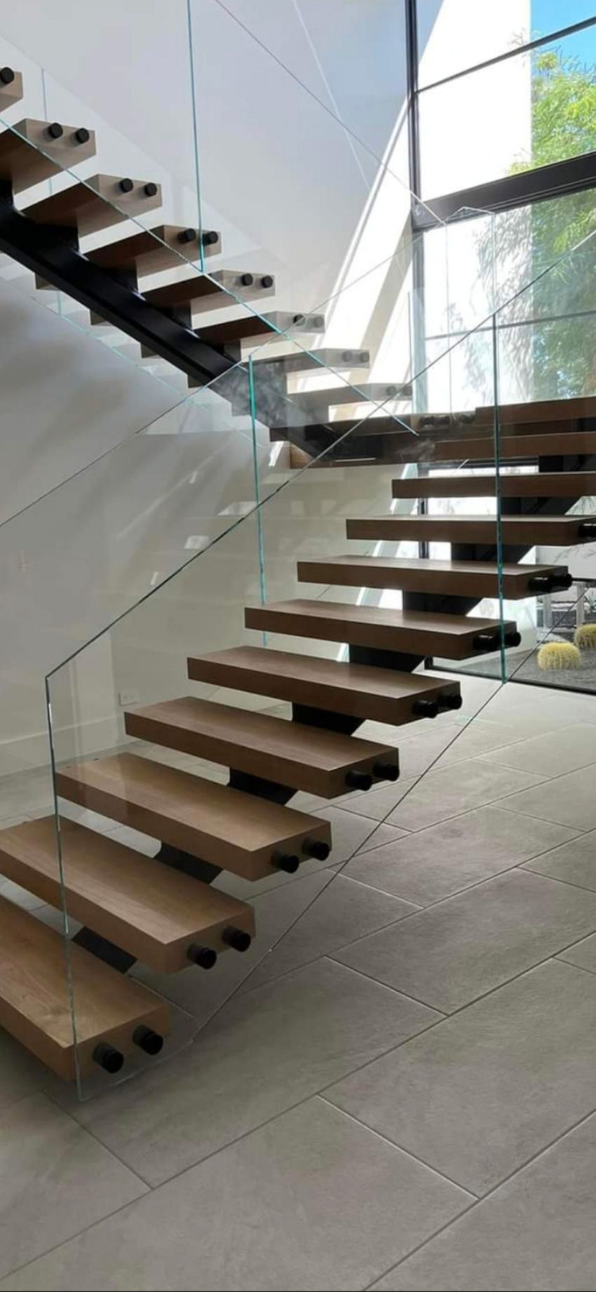 A black metal staircase with glass railings sits behind a black sofa and potted snake plants in a modern interior.