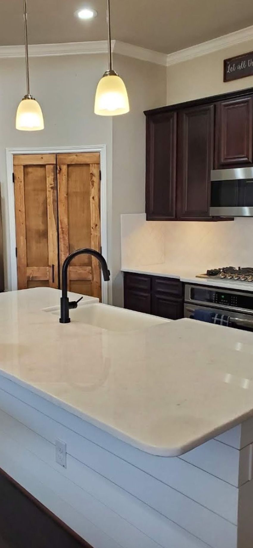 A kitchen island with a white countertop and black faucet, featuring dark cabinets and rustic wooden doors in the back.