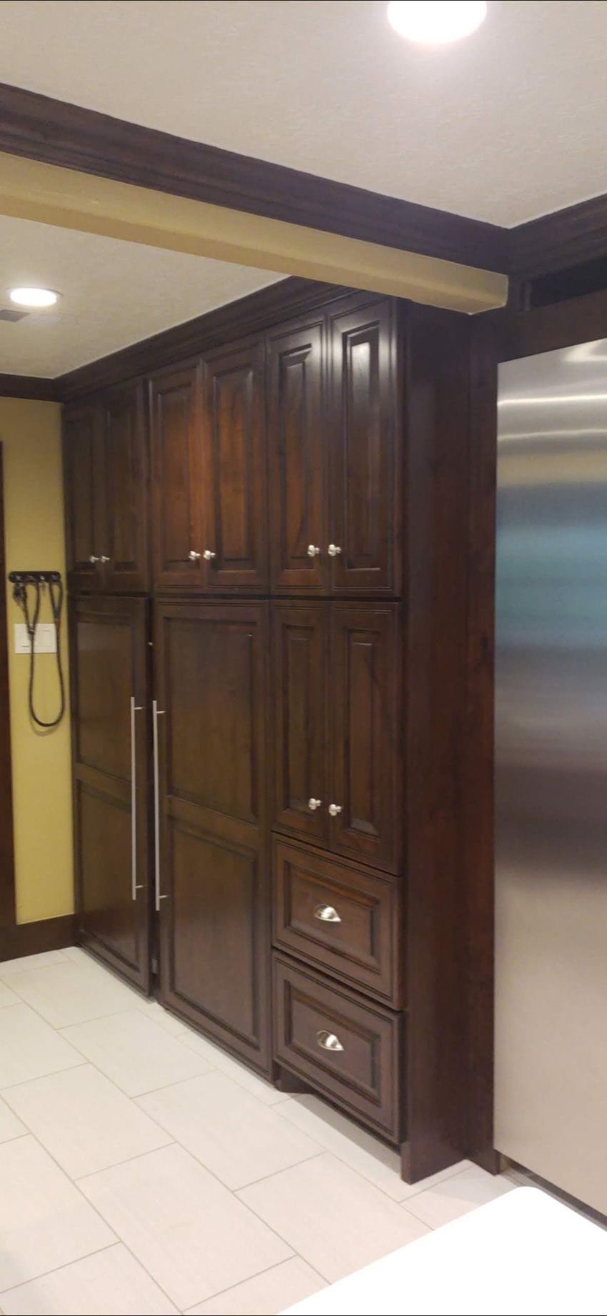 Tall, dark wood kitchen cabinetry featuring built-in storage cabinets and drawers beside a stainless steel refrigerator.