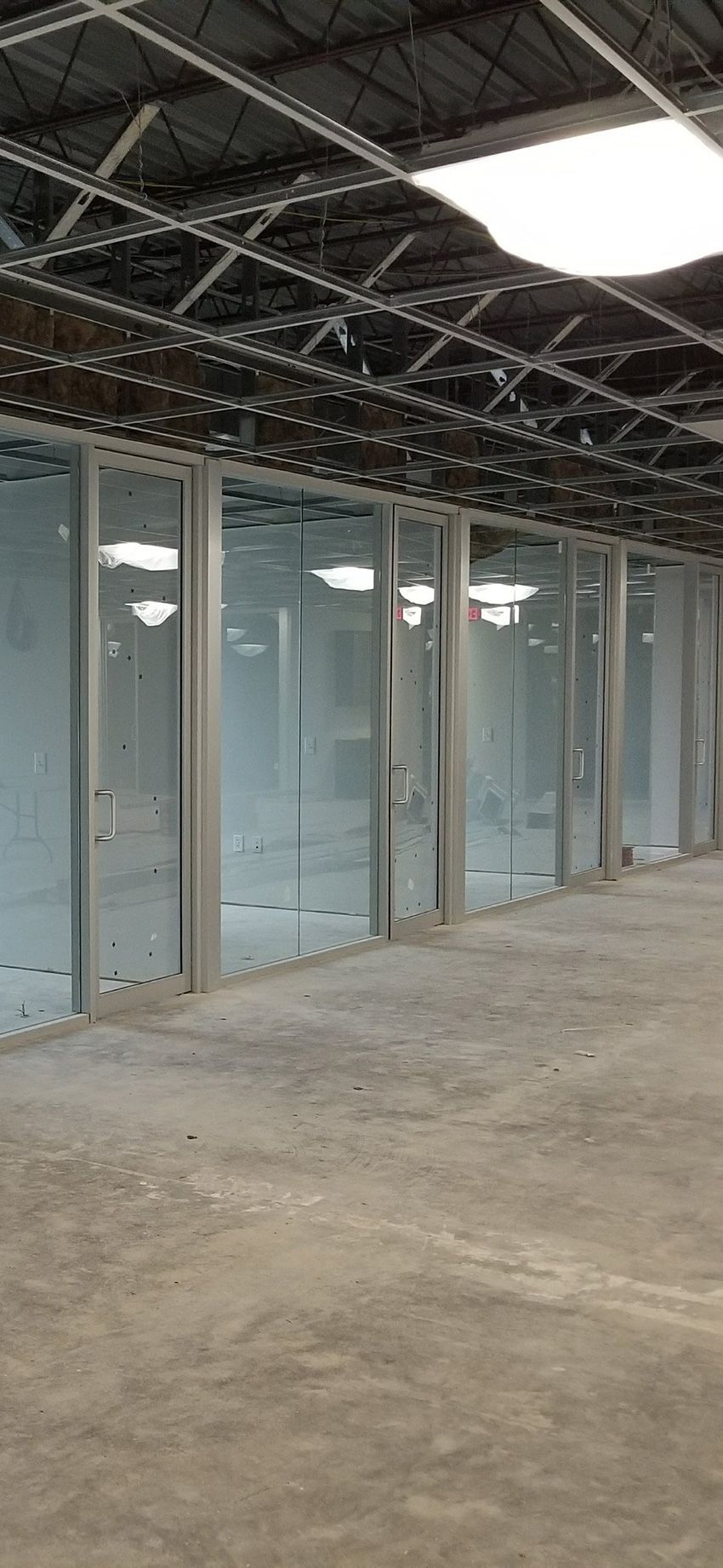A modern office interior under construction with glass partitions, metal framing, and an unfinished ceiling.