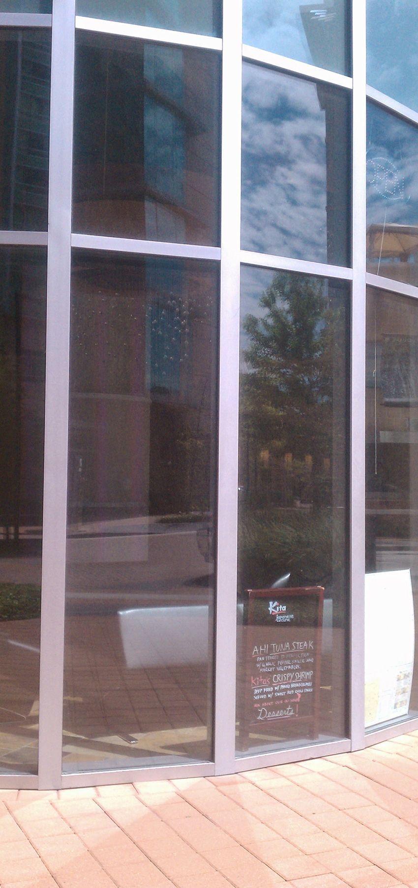 A curved, floor-to-ceiling glass storefront with reflections of trees and buildings, and a small sign in the window.