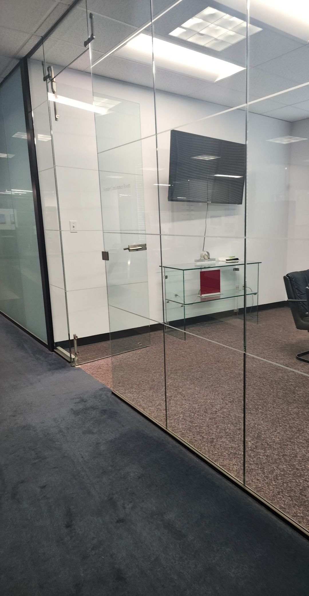 A modern office conference room with glass walls, a wall-mounted TV, and a white console table.