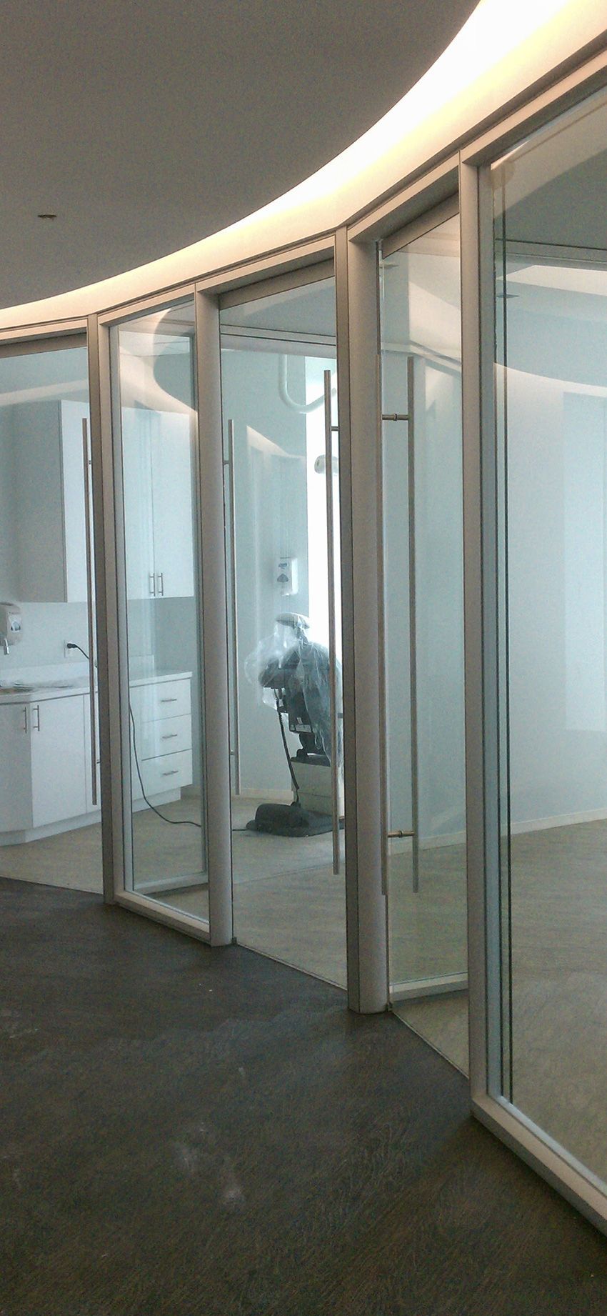 A series of glass-paneled doors with white frames create a curved wall in a brightly lit, modern office space.
