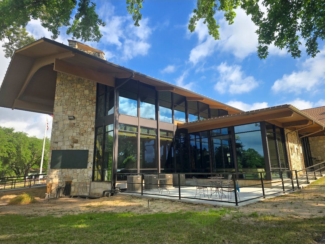 Modern building with a stone chimney and large glass windows under a blue sky with scattered clouds.