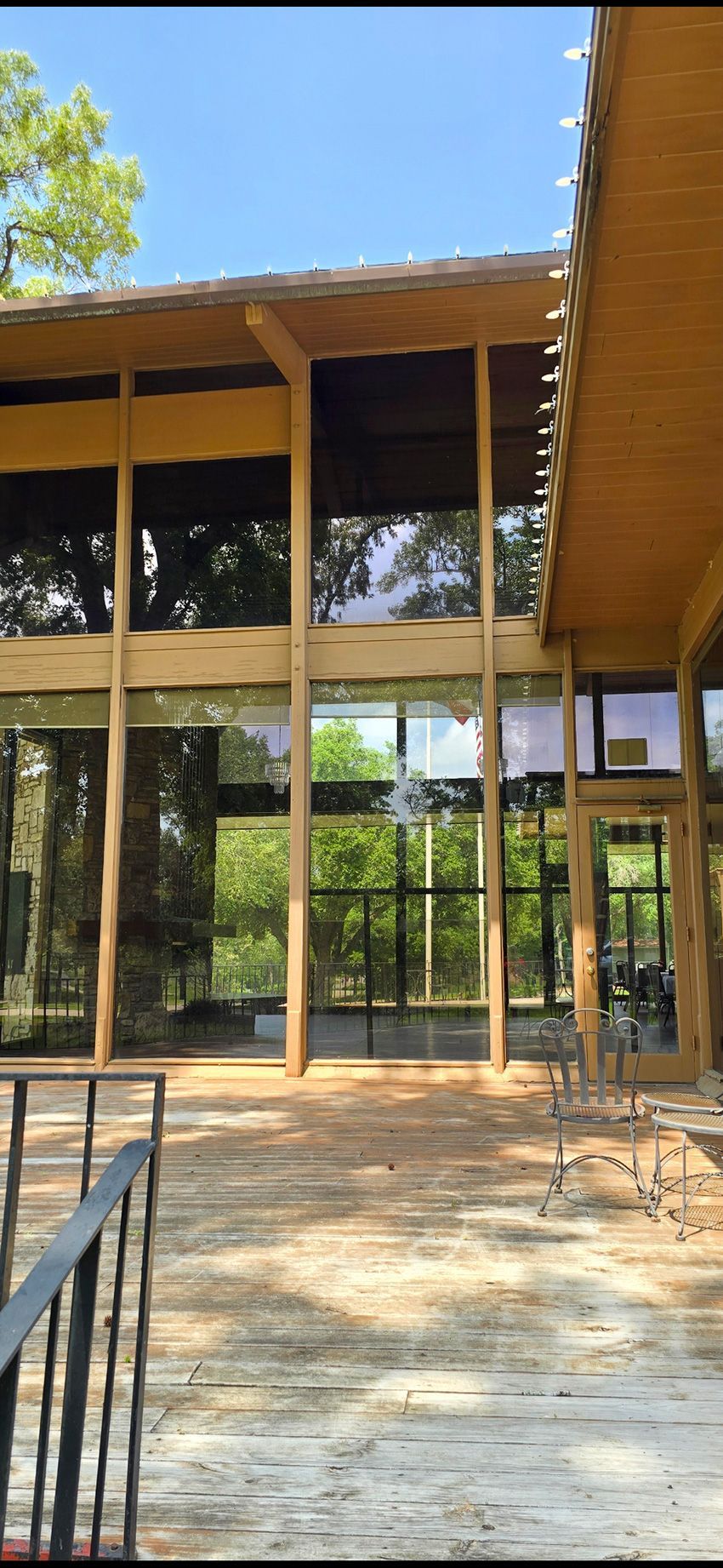 A patio with a stone floor looks out toward a two-story building with large glass windows and wooden structural beams.