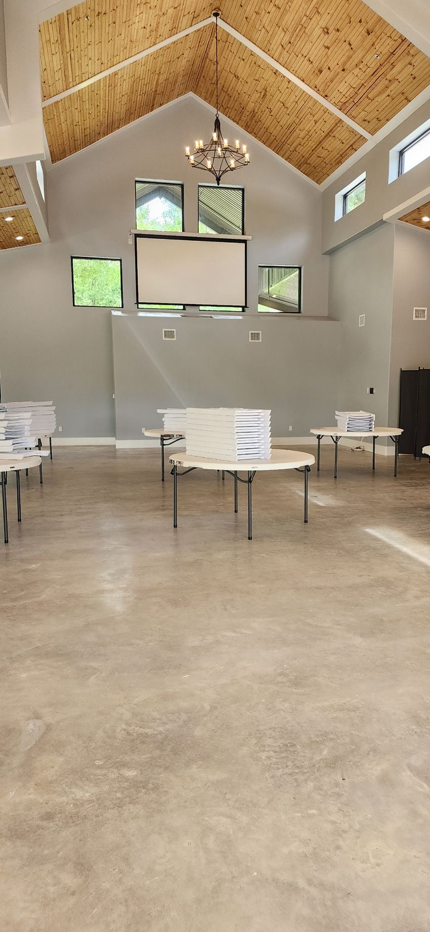 An interior view of a room set up for voting with privacy screens on round tables, concrete floors, and a vaulted ceiling.