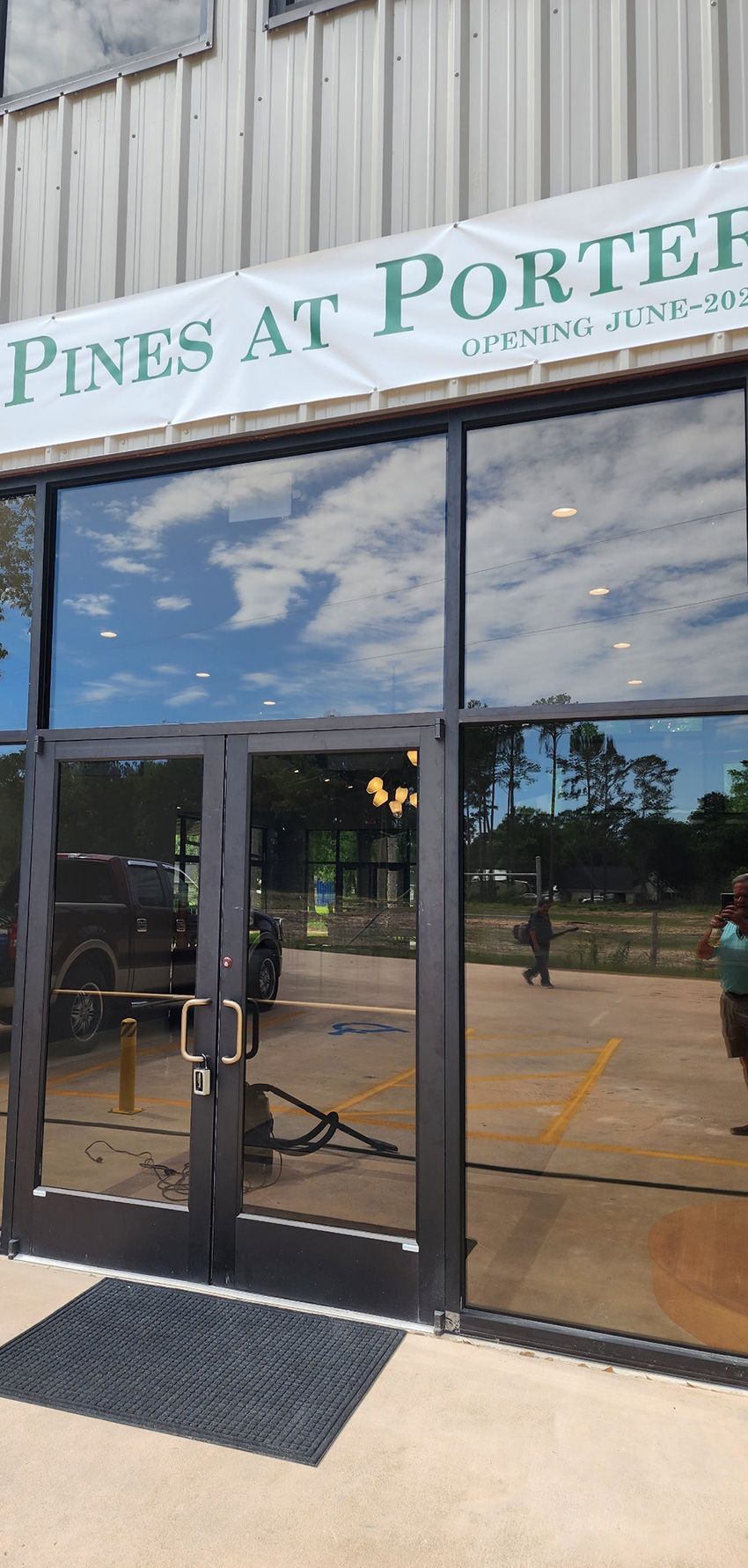 Glass double doors at the Pines at Porter apartment leasing office, with a reflected parking lot visible in the windows.