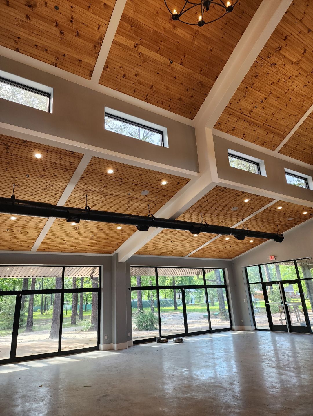 A bright, modern indoor event space featuring a high, sloped wood ceiling, large glass windows, and concrete floors.