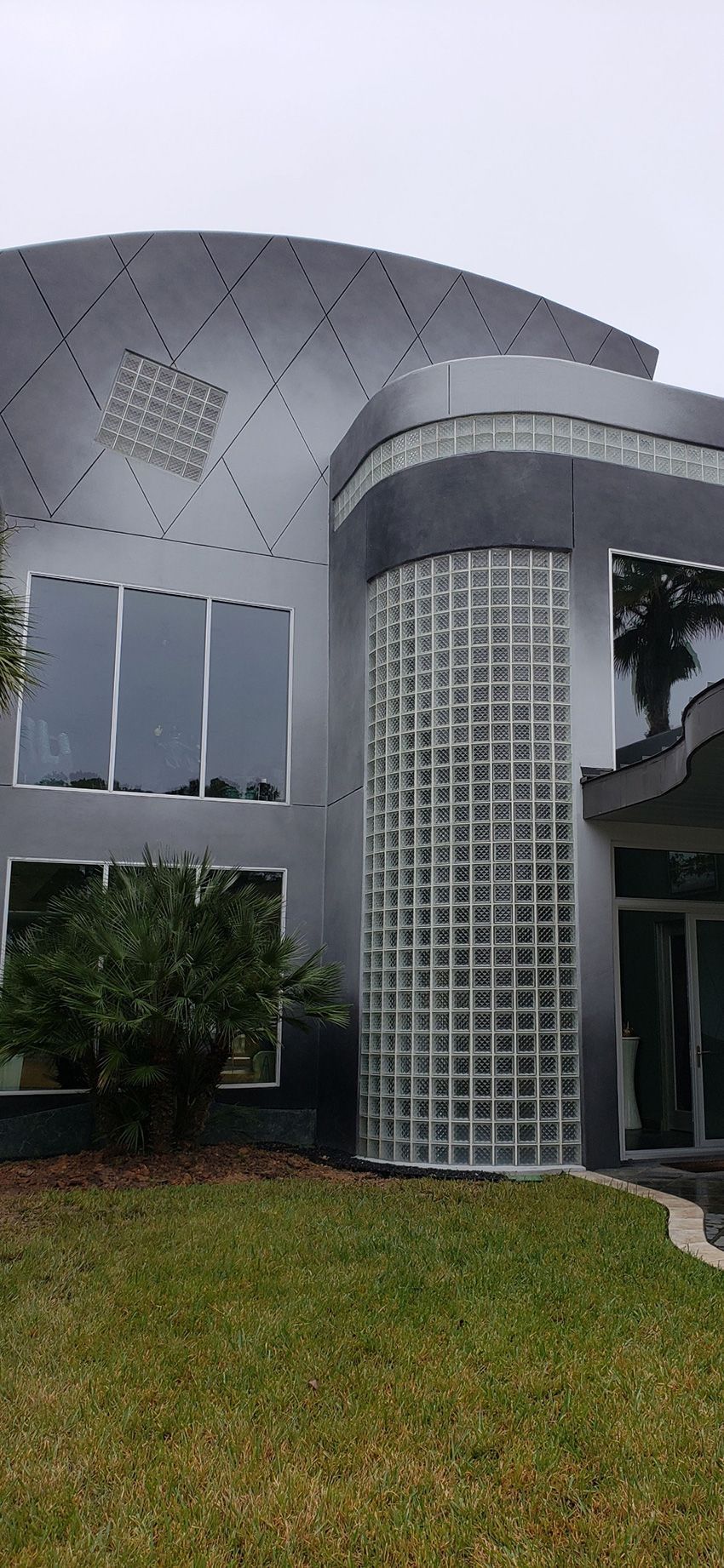 A modern two-story home with a curved gray facade, a glass block wall, and dark-tinted windows.