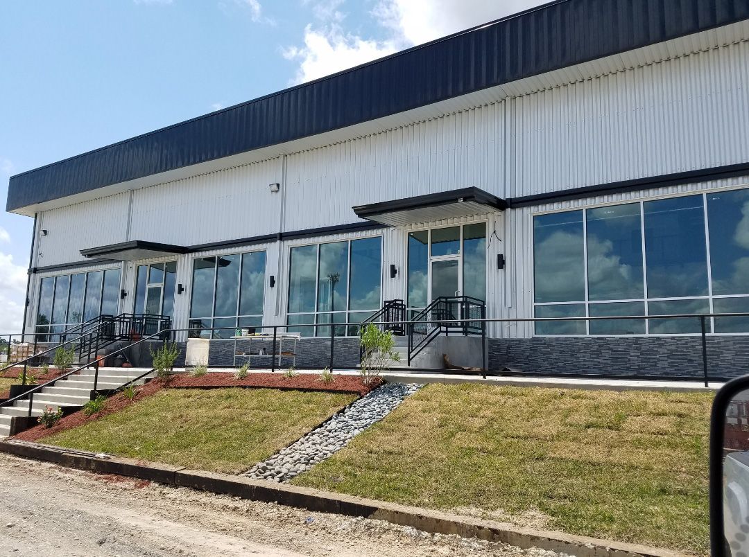 A modern, white, industrial-style commercial building with large glass windows, a dark roof, and a stone-tiled base.
