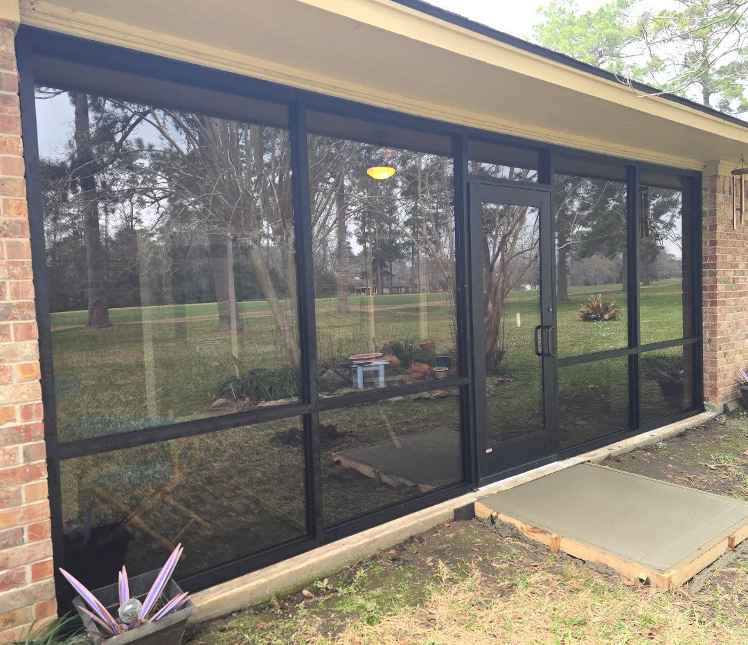 A wall of dark-framed floor-to-ceiling glass windows and a door looking out onto a grassy, wooded yard.