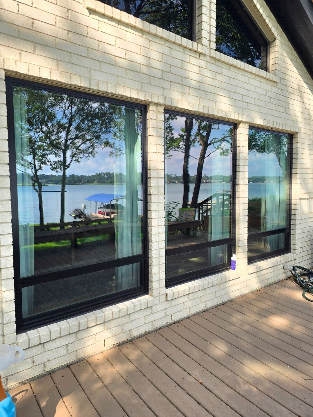 A view of a lake and deck reflected in large floor-to-ceiling windows on a white brick house.