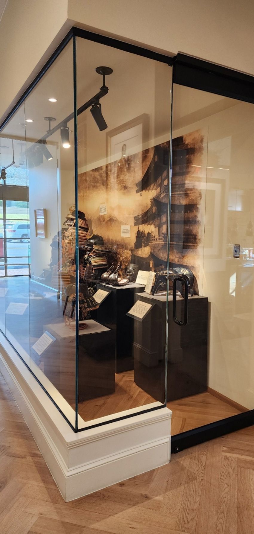 A glass display case in a gallery containing pedestals with artifacts and a large abstract print on the wall behind.