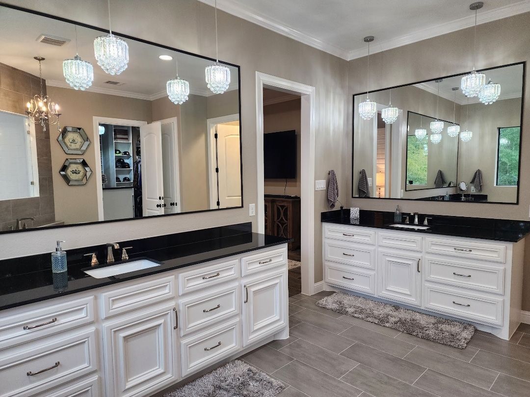 A bright bathroom featuring two white vanities with black countertops, large mirrors, crystal pendant lights, and tile floors.